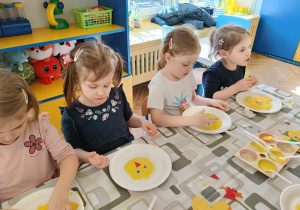 dzieci siedzą przy stolikach, doklejają elementy kurczakom