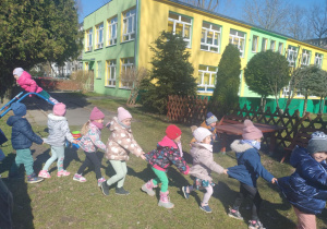 dzieci tworzą pociąg i maszerują po ogrodzie przedszkolnym