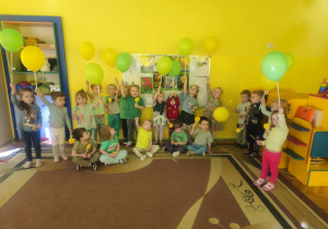 dzieci trzymają w ręku balony oraz kwiatki i pozują do zdjęcia grupowego