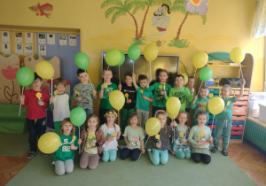 dzieci trzymają w ręku balony oraz kwiatki i pozują do zdjęcia grupowego