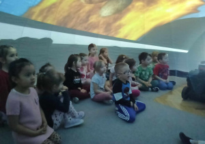 dzieci siedzą w środku mobilnego planetarium słuchają i oglądają multimedialną prezentację