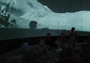 dzieci znajdują się w środku mobilnego planetarium słuchają i oglądają multimedialną prezentację