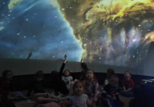 dzieci znajdują się w środku mobilnego planetarium słuchają i oglądają multimedialną prezentację