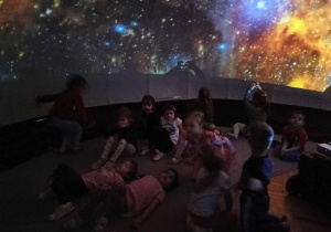 dzieci znajdują się w środku mobilnego planetarium słuchają i oglądają multimedialną prezentację