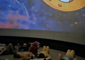 dzieci znajdują się w środku mobilnego planetarium słuchają i oglądają multimedialną prezentację