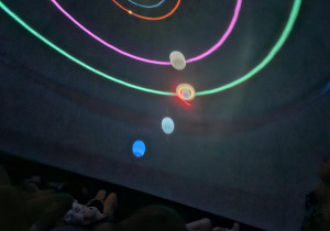 dzieci znajdują się w środku mobilnego planetarium słuchają i oglądają multimedialną prezentację