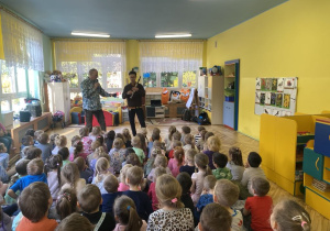 dzieci tańczą na dywanie, słuchając muzyka który gra na saksofonie.