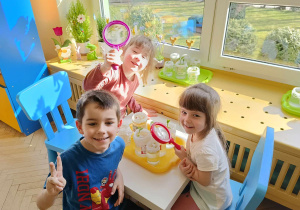 3 dzieci obserwuje przez lupy wzrost fasoli