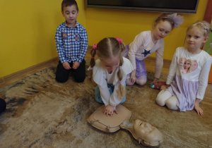 Dziewczynka z grupy srebrnej wykonuje uściśnięcia klatki piersiowej na fantomie.