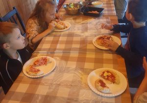 Dzieci jedzą przygotowane przez siebie pizze