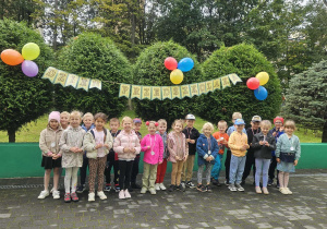 Dzieci stoją na tarasie przedszkolnym, pozują do zdjęcia grupowego