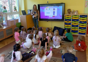 prowadząca objaśnia dzieciom wykonanie zadania na monitorze edukacyjnym