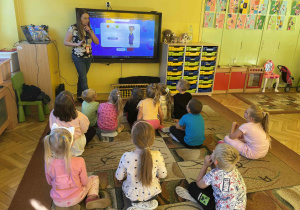 prowadząca objaśnia dzieciom wykonanie zadania na monitorze edukacyjnym