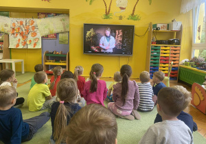 dzieci siedzą na dywanie oglądając film