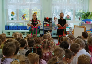tancerze prezentują tańce ludowe, dzieci siedzą w sali przyglądając się ich tanecznym popisom
