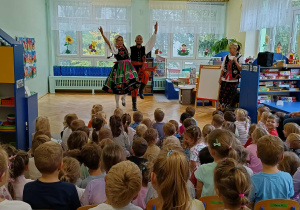 tancerze prezentują tańce ludowe, dzieci siedzą w sali przyglądając się ich tanecznym popisom