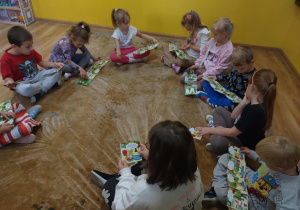 Dzieci siedzą na dywanie i oglądają ilustrowana instrukcje jak krok po kroku wykonać pierwsza pomoc