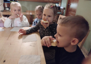 Dzieci siedzą przy stołach i delektują się słodkim ciasteczkiem.