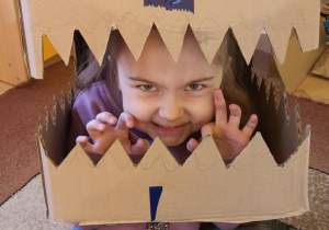 dziewczynka przymierza głowę dinozaura wykonaną z kartonu