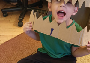 Chłopiec przymierza głowę dinozaura wykonaną z kartonu