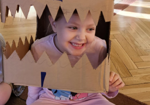 dziewczynka przymierza głowę dinozaura wykonaną z kartonu