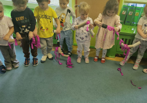 Dzieci w kole przeciągają rolki po sznurku.