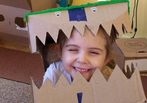 dziewczynka przymierza głowę dinozaura wykonaną z kartonu