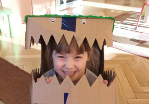 dziewczynka przymierza głowę dinozaura wykonaną z kartonu