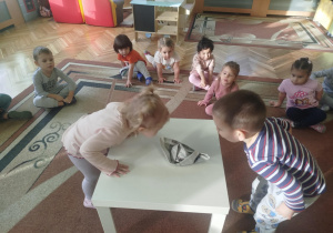 Dzieci biorą udział w ćwiczeniach oddechowych dmuchając na łódkę zrobiona z gazety