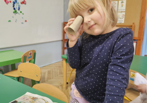 Dziewczynka wyszukuje elementów obrazka za pomocą lornetki z rolki.