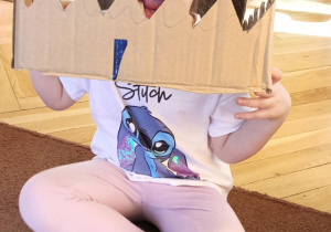 dziewczynka przymierza głowę dinozaura wykonaną z kartonu