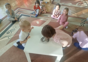 Dzieci biorą udział w ćwiczeniach oddechowych dmuchając na łódkę zrobiona z gazety