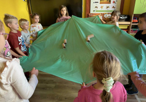 dzieci poruszają folią malarską i rolkami po papierze podczas zabawy „falujące morze”