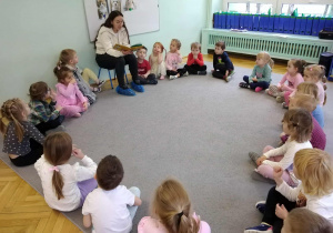 Dzieci siedzą w kole i słuchają czytane książki.