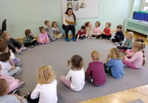 Dzieci siedzą w kole i słuchają czytane książki.