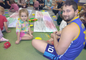 Rodzice i dzieci siedzą na dywanie. Na środku leżą zrobione przez rodziców sieci pajęcze.