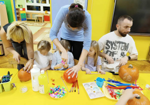 dzieci wraz z rodzicami ozdabiają dynie