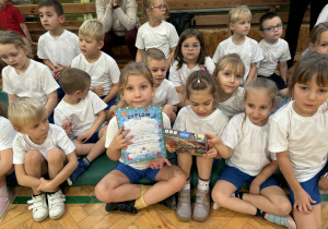 dzieci siedzą na materacach i prezentują dyplomy i nagrody otrzymane podczas zawodów