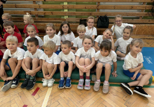 dzieci z grupy srebrnej i czerwonej siedzą na materacach i słuchają poleceń prowadzącego zawody nauczyciela