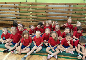 dzieci z grupy srebrnej i czerwonej siedzą na materacach i słuchają poleceń prowadzącego zawody nauczyciela