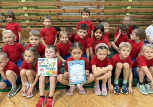 dzieci siedzą na materacach i prezentują dyplomy i nagrody otrzymane podczas zawodów