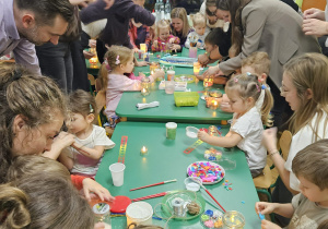 Rodzice ppmagają dzieciom zrobić lampiony ze słoików.