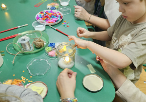 Rodzice ppmagają dzieciom zrobić lampiony ze słoików.