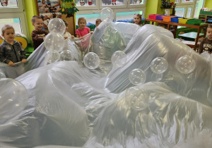 Dzieci trzymają folię malarską i podrzucają balony.