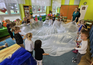 Dzieci trzymają folię malarską i podrzucają balony.