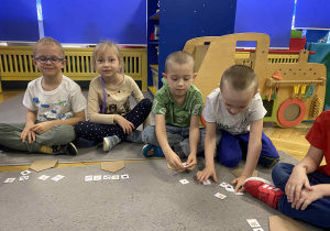 Dzieci siedzą na dywanie naklejają naklejki