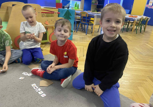 Dzieci siedzą na dywanie naklejają naklejki