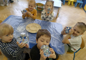 Dzieci wykonują serca - wrzucają pompony, brokat, błękitne i białe cekiny