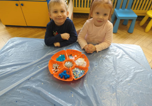 Dzieci wykonują serca - wrzucają pompony, brokat, błękitne i białe cekiny