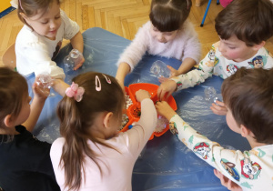 Dzieci wykonują serca - wrzucają pompony, brokat, błękitne i białe cekiny